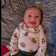 Creed is registered to the contest to win money with this photo: baby, smiling, infant, child, cute, koala_print, clothing, blanket, happy, portrait, lying_down, face, cheerful, indoors, soft_lighting, head, person, sleeve, fabric, cozy
