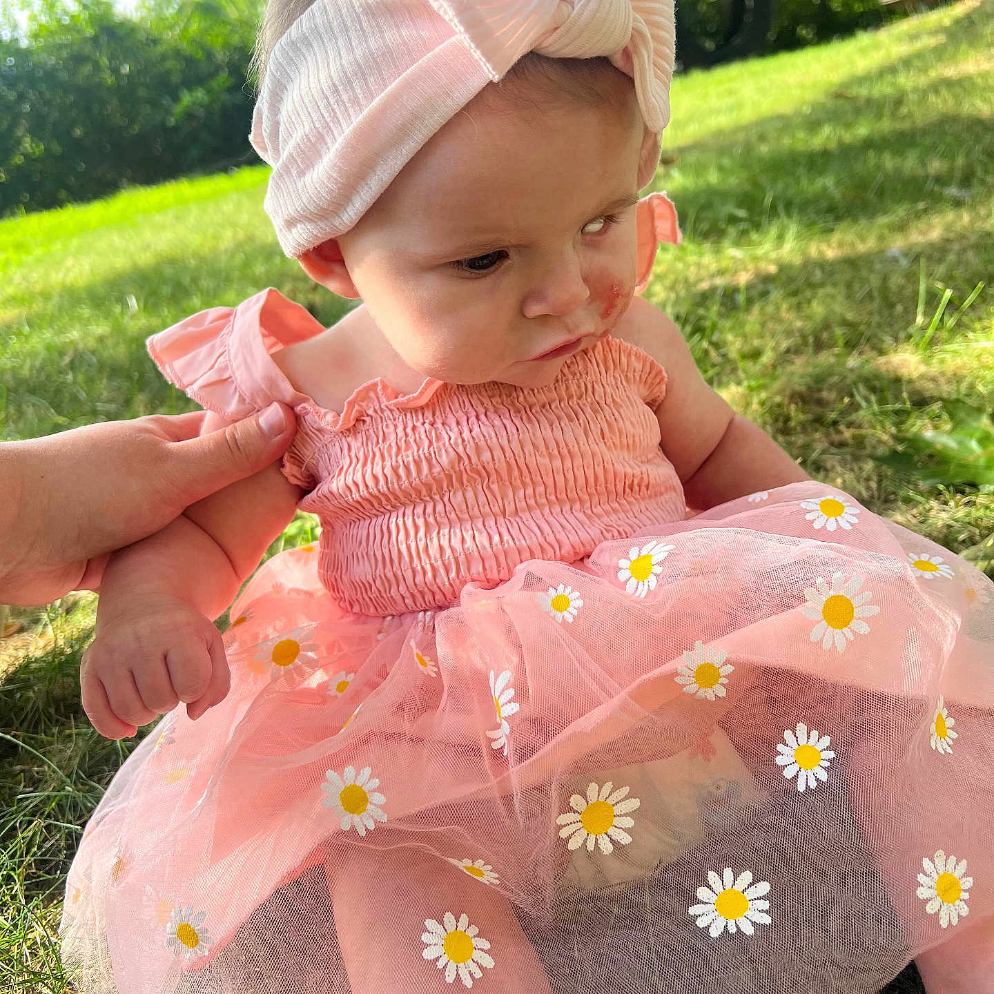 Peyton is registered to the contest to win money with this photo: baby, bow, child, curious, cute, face, flower_pattern, grass, greenery, hand, headband, infant, nature, outdoor, person, pink_dress, sitting, summer, sunlight, support