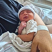 Noel is registered to the contest to win money with this photo: newborn, baby, infant, hat, blanket, hospital, hospital_bed, person, hand, sleeping, resting, clothing, skin, arm, comfort, cute, cozy, portrait, indoor, care