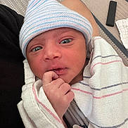 Noel is registered to the contest to win money with this photo: newborn, baby, infant, wrapped, blanket, hat, striped_hat, hospital, person, hand, face, eyes, indoor, carpet, floor, resting, cute, small, cozy, portrait