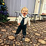 child, toddler, smiling, indoor, carpet, clothing, shoes, sneakers, christmas_tree, decorations, table, window_blinds, curtains, person, happy, standing, patterned_floor, holiday, room, curly_hair