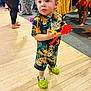 toddler, child, person, clothing, toy, floor, indoor, party, people, footwear, socks, patterned_clothing, colorful, curly_hair, standing, holding, background, legs, festival, celebration