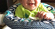 Antonio is registered to the contest to win money with this photo: baby, smiling, infant, baby_seat, green_clothing, indoor, living_room, furniture, carpet, patterned, happy, child, cute, person, seat, home, decor, cross, portrait, sitting