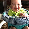 baby, smiling, infant, baby_seat, green_clothing, indoor, living_room, furniture, carpet, patterned, happy, child, cute, person, seat, home, decor, cross, portrait, sitting