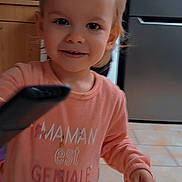 Laurianna a rejoint le concours — aidez-le/la à gagner de superbes lots ! blond_hair, cabinet, casual_clothing, child, curious, cute, face, floor_tiles, home, indoor, kitchen, person, pink_shirt, portrait, refrigerator, remote_control, small_hand, smile, toddler, young_child