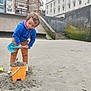 child, sand, beach, shovel, bucket, blue_jacket, brown_pants, urban, building, concrete, stairs, playing, outdoor, sandcastle, toy, young_child, casual_clothing, daytime, fun, concentration