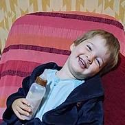 Khyako a rejoint le concours — aidez-le/la à gagner de superbes lots ! child, smiling, bottle, chair, striped, pink, orange, blue_clothing, happy, indoor, person, young_child, face, hair, jacket, relaxed, candid, portrait, cozy, furniture