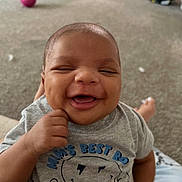 Hezakiah is registered to the contest to win money with this photo: baby, smiling, happy, infant, indoor, tshirt, face, child, person, cute, joyful, carpet, ball, blurred_background, thumbs_up, casual_clothing, head, young_child, closeup, sitting