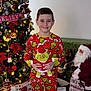 Caden joined the competition — help win amazing prizes! child, pajamas, grinch, plush_toy, christmas_tree, holiday_decorations, gift_bags, santa_figure, sign, flooring, smile, standing, indoors, festive, red_clothing, yellow_trim, barefoot, lights, ornaments, holiday