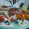 baby, child, blue_hat, baby_walker, outdoor, toy, grass, tree, daylight, curious, face, infant, playtime, nature, person, park, sunny, headwear, grass_field, early_spring
