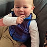baby, child, smiling, sitting, couch, blanket, vest, long_sleeve, pants, furniture, indoor, table, soda_can, mug, face, hand, happy, cozy, portrait, cute
