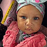 Madison is registered to the contest to win money with this photo: baby, child, infant, headband, pink, vest, car_seat, seatbelt, face, portrait, clothing, floral, cute, sitting, young_child, indoor, warning_label, closeup, person, expression