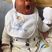 Aayan is registered to the contest to win money with this photo: baby, infant, yawning, bib, pajamas, mickey_mouse, donald_duck, goofy, clothing, white_mittens, hat, couch, blanket, towel, indoor, person, cute, expression, child, sitting