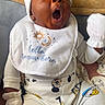 baby, infant, yawning, bib, pajamas, mickey_mouse, donald_duck, goofy, clothing, white_mittens, hat, couch, blanket, towel, indoor, person, cute, expression, child, sitting