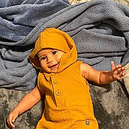 Eris joined the competition — help win amazing prizes! baby, child, hood, romper, blanket, bedding, smile, cute, arm, hand, eye_contact, portrait, indoor, cozy, mustard_color, textile, button, laying, soft, fabric
