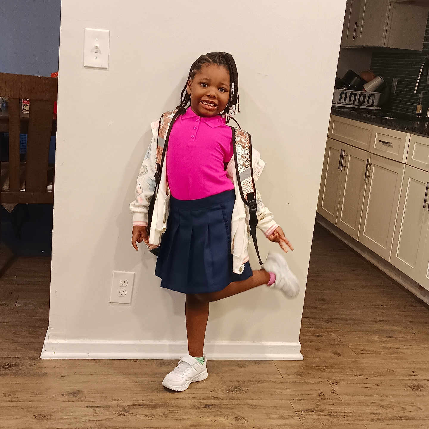 Zatressa is registered to the contest to win money with this photo: backpack, braided_hair, cabinet, carpet, child, dining_chair, girl, happy, home, indoor, jacket, kitchen, light_switch, navy_skirt, pink_shirt, pose, power_outlet, smiling, white_shoes, wood_floor