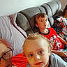 child, toddler, adult, couch, indoor, casual, family, portrait, curly_hair, red_shirt, glasses, relaxed, living_room, blanket, seated, curious, young_child, home, people, cozy
