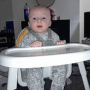 Leo is registered to the contest to win money with this photo: baby, high_chair, onesie, animal_print, indoor, living_room, mirror, pepsi_bottle, carpet, furniture, child, person, seat, hands, face, expression, cute, decor, bottle, footwear