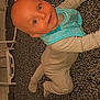 baby, child, crawling, carpet, floor, onesie, bib, indoor, furniture, chair, table, smiling, face, head, person, young_child, cute, looking_up, carpeted_floor, home