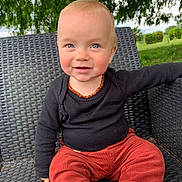 Mattìa a rejoint le concours — aidez-le/la à gagner de superbes lots ! toddler, child, smiling, outdoor, chair, woven_chair, black_shirt, red_pants, necklace, amber, blue_eyes, portrait, cute, happy, grass, trees, nature, casual_clothing, sitting, baby