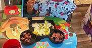 Aiden is registered to the contest to win money with this photo: child, boy, mickey_mouse, table, food, plate, chair, cup, meal, shirt, indoor, floor, expression, happy, cute, kid, colorful, dining, snack, playful