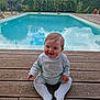 Lyam participe au concours pour gagner de l'argent avec cette photo : baby, child, smiling, sitting, pool, water, wooden_deck, outdoor, nature, greenery, sky, clouds, reflection, plants, hedge, daylight, cute, infant, clothing, happy