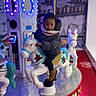 amusement_ride, boots, carousel, child, coat, decorative, face, family_fun, indoor, kid, led_lights, merry_go_round, person_peeking, platform, play, portrait, red_carpet, scarf, smile, toy_horse