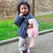 Hilona participe au concours pour gagner de l'argent avec cette photo : child, curly_hair, cute, grass, hand_on_face, happy, jacket, outdoor, pants, park, plush_bunny, portrait, sidewalk, smiling, sneakers, standing, stone_wall, stuffed_animal, toy, tree