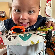 Jeremiah is registered to the contest to win money with this photo: baby, child, smiling, face, eyes, activity_center, toy, orange_ring, yellow_ring, clothing, indoor, furniture, santa_decoration, holiday, happy, cute, person, infant, playtime, closeup