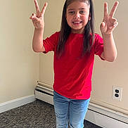 Athena Joseph is registered to the contest to win money with this photo: child, girl, smiling, red_shirt, jeans, peace_sign, long_hair, indoor, carpet, wall, power_outlet, posing, happy, casual_clothing, standing, young, person, portrait, home, fun