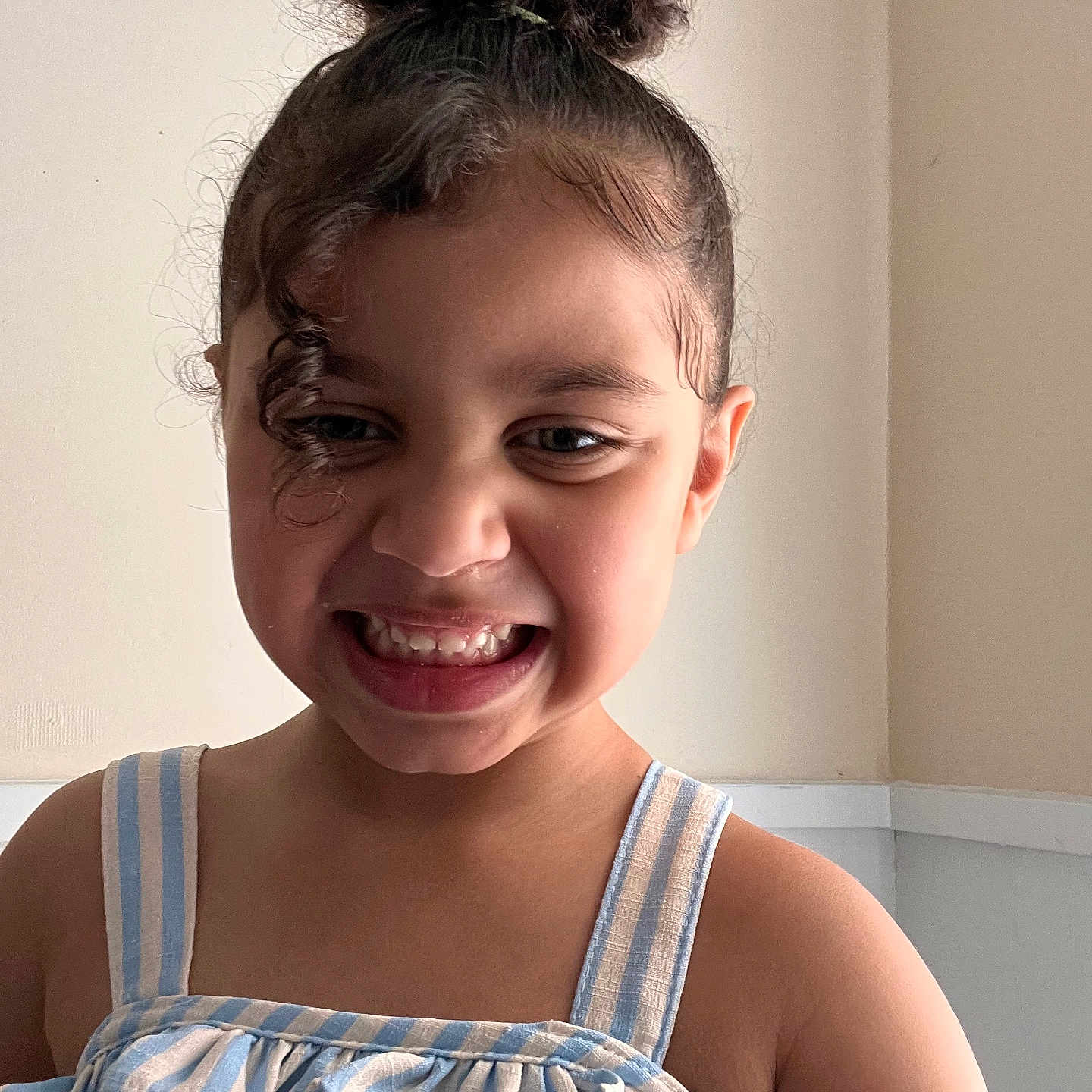 Athena Joseph is registered to the contest to win money with this photo: child, smiling, portrait, hair_bun, curly_hair, striped_clothing, tank_top, happy, indoor, person, face, young_child, casual_wear, cute, light_skin, wall, natural_light, closeup, fashion, expression