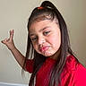 Athena Joseph is registered to the contest to win money with this photo: child, girl, long_hair, red_shirt, pouty_face, hand_gesture, peace_sign, indoor, carpet, wall, casual_clothing, portrait, expression, hair_clip, young, person, cute, playful, standing, light_skin