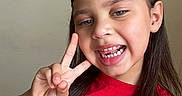 Athena Joseph is registered to the contest to win money with this photo: child, girl, smile, peace_sign, red_shirt, long_hair, missing_teeth, portrait, happy, casual, indoor, person, face, hand, gesture, hair_tie, young, cute, friendly, skin