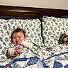 Vincent is registered to the contest to win money with this photo: baby, bed, blanket, child, comfort, cozy, cute, dog, floral_pattern, home, indoor, pet, pillow, quilt, resting, sleeping, sleepwear, smiling, toddler, wooden_headboard