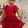 child, girl, red_dress, indoor, playful, face_stickers, pink_bows, wooden_floor, chair, decorated_house, window, curtains, smiling, person, home, floor, furniture, cute, posing, young
