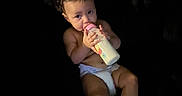 Alexia is registered to the contest to win money with this photo: baby, bottle, diaper, drinking, infant, child, milk, cute, face, feet, hands, skin, dark_background, lighting, portrait, young_child, alone, indoor, candid, expression