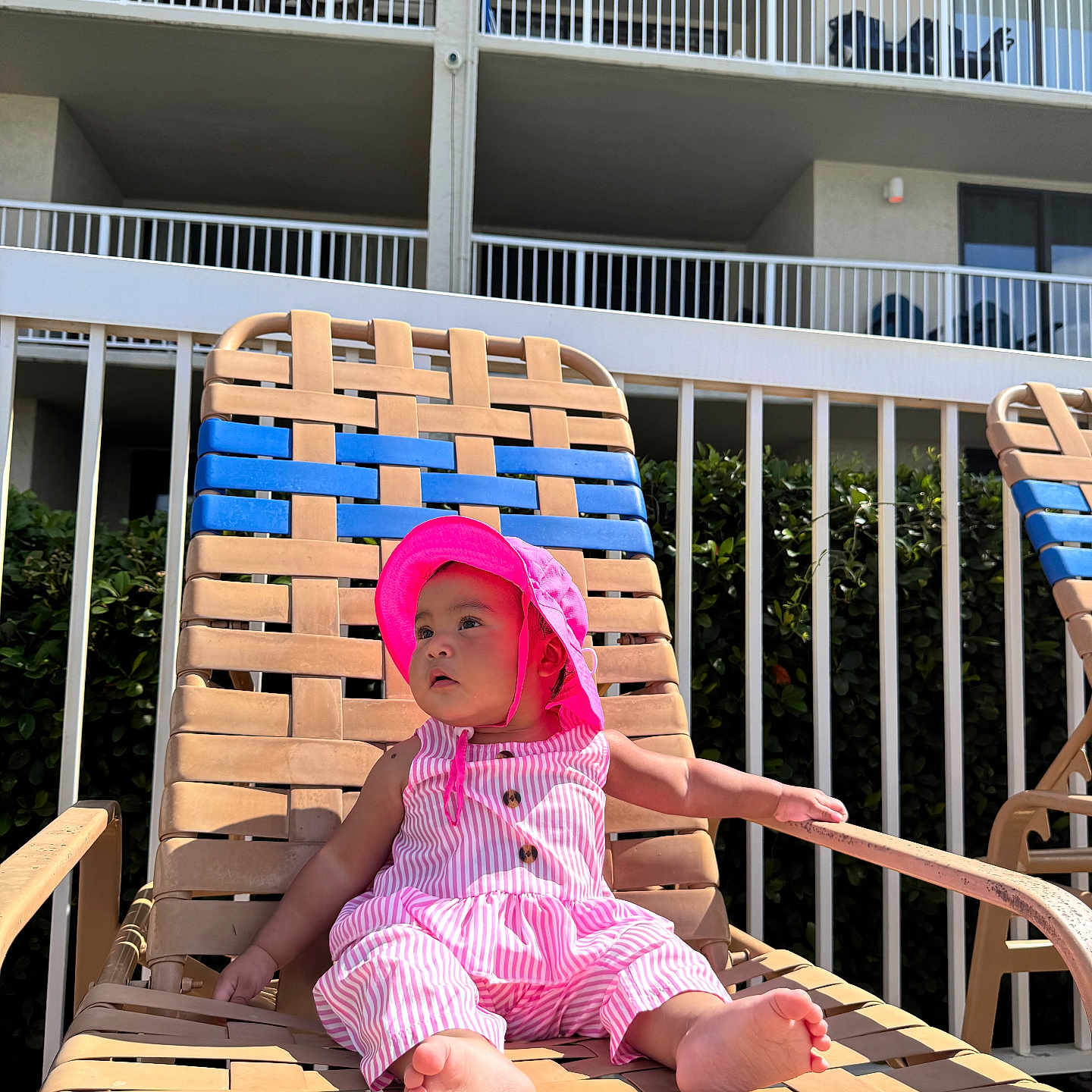 Arleth Lopez is registered to the contest to win money with this photo: baby, balcony, barefoot, casual_clothing, child, curious, daylight, greenery, infant, outdoor, pink_hat, pink_outfit, pool_chair, relaxing, residential_building, summer, sunhat, sunshine, woven_chair, young_child