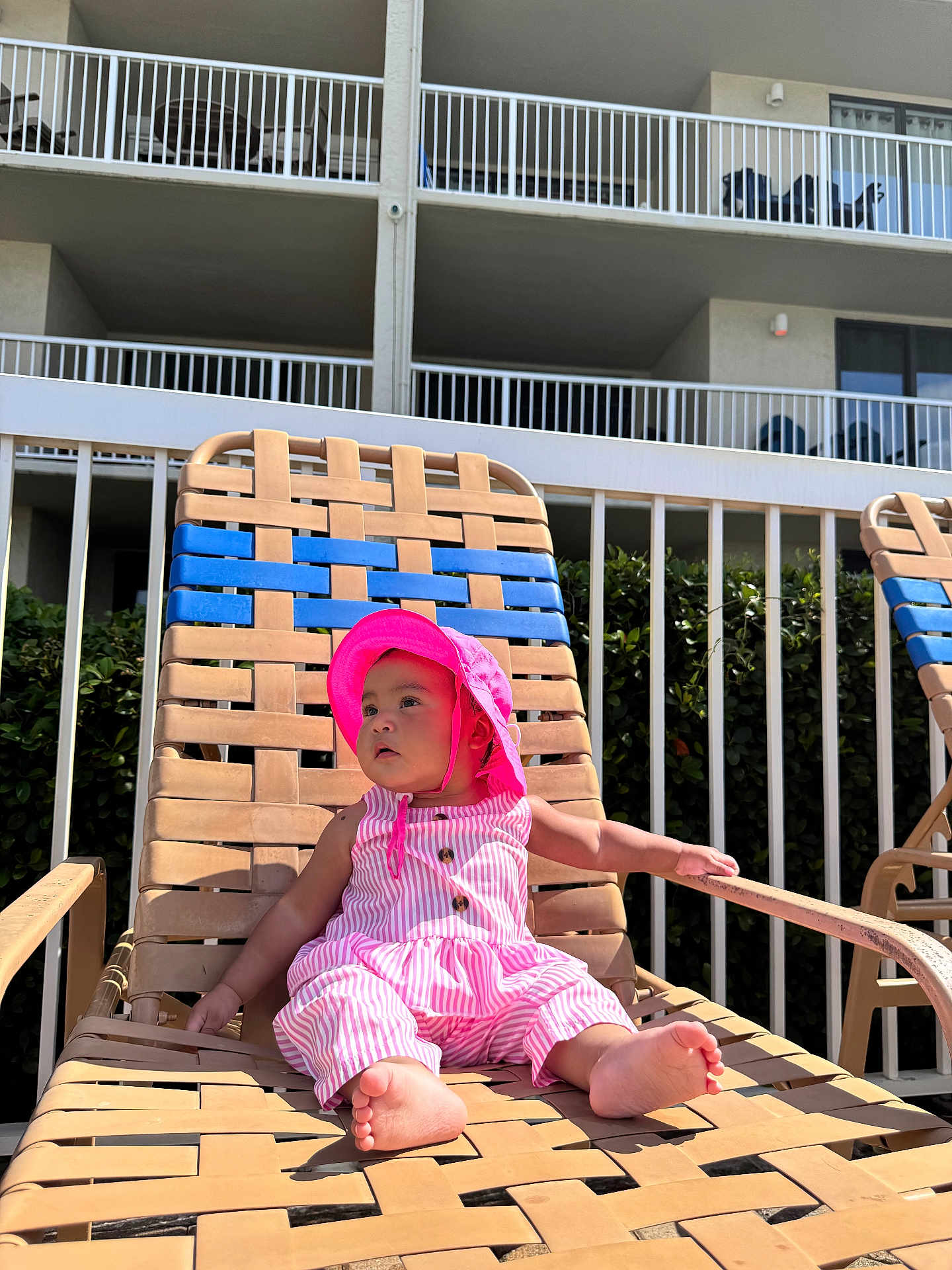 Arleth Lopez is registered to the contest to win money with this photo: baby, child, pink_hat, pink_outfit, sunhat, pool_chair, woven_chair, outdoor, daylight, residential_building, balcony, greenery, curious, relaxing, summer, sunshine, barefoot, infant, casual_clothing, young_child