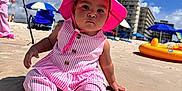 Arleth Lopez joined the competition — help win amazing prizes! child, toddler, beach, sand, sunhat, pink_clothing, striped_outfit, barefoot, umbrella, sky, clouds, building, outdoor, vacation, summer, sunshine, person, playing, water_toy, relaxation