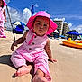 barefoot, beach, building, child, clouds, outdoor, person, pink_clothing, playing, relaxation, sand, sky, striped_outfit, summer, sunhat, sunshine, toddler, umbrella, vacation, water_toy