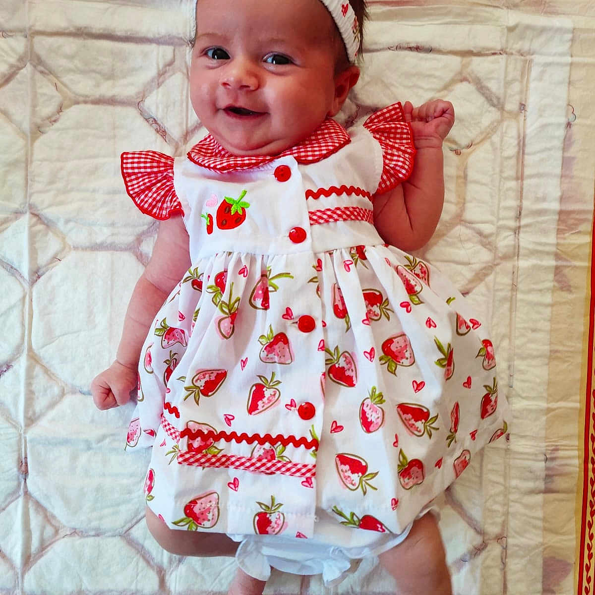 Ambre a rejoint le concours — aidez-le/la à gagner de superbes lots ! baby, baby_girl, blanket, child, clothing, cute, dress, fabric, happy, headband, indoors, infant, lying_down, pattern, person, portrait, red, smiling, strawberry_pattern, white