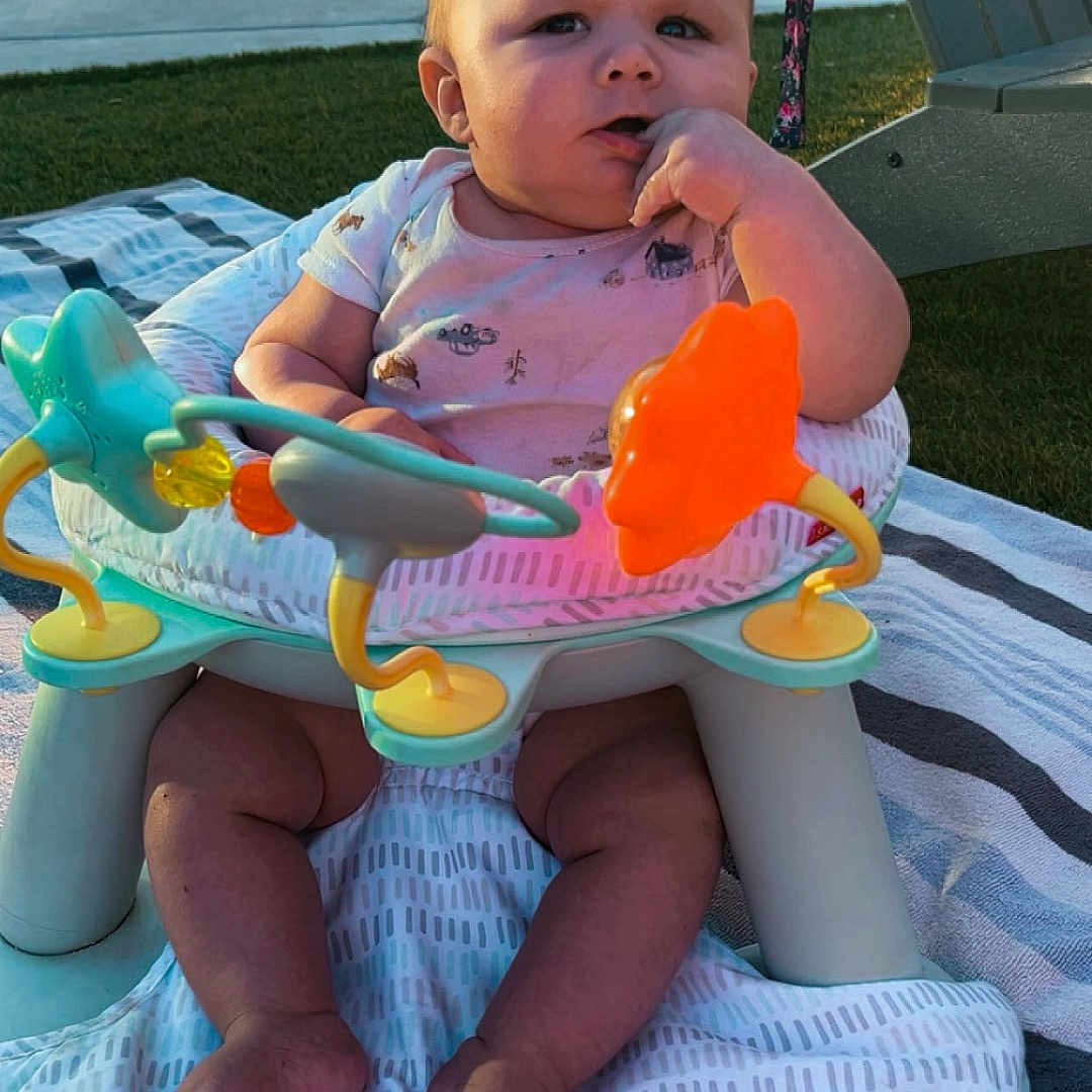 Weston is registered to the contest to win money with this photo: baby, child, outdoor, activity_seat, toy, blanket, grass, person, infant, cute, summer, playtime, footwearless, sitting, expression, colorful, sunlight, relaxing, garden, daytime