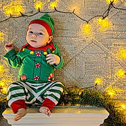 Adrian joined the competition — help win amazing prizes! baby, infant, child, elf_costume, green_clothing, red_clothing, striped_pants, holiday, christmas_lights, fairy_lights, carpet, floor, festive, cute, indoors, portrait, smiling, holiday_decor, feet, hat