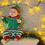baby, infant, child, elf_costume, green_clothing, red_clothing, striped_pants, holiday, christmas_lights, fairy_lights, carpet, floor, festive, cute, indoors, portrait, smiling, holiday_decor, feet, hat