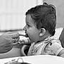 baby, bib, black_and_white, child, closeup, cute, eating, feeding, hand, high_chair, indoor, infant, keys, mouth_open, person, portrait, rings, spoon, table, wet_hair