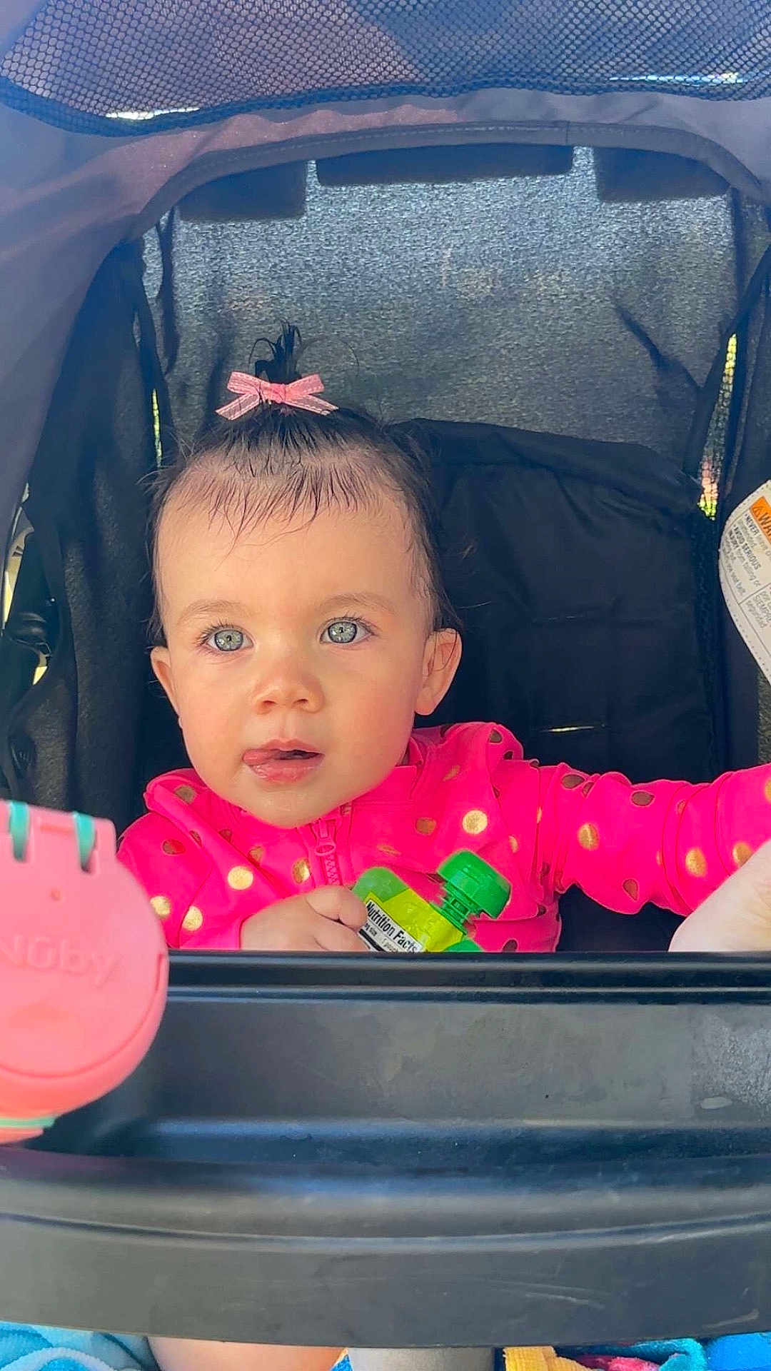 Azlynn is registered to the contest to win money with this photo: toddler, child, stroller, pink_jacket, bow, blue_eyes, snack_pouch, curious, baby, outdoor, playful, face, hands, clothing, seat, person, portrait, infant, cute, expression