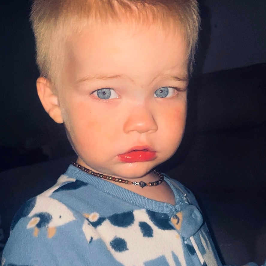 Canaan is registered to the contest to win money with this photo: baby, blond_hair, blue_eyes, child, close_up, clothing, cow_pattern, curious, cute, dark_background, expression, face, indoor, necklace, onesie, pajamas, person, portrait, toddler, young_child