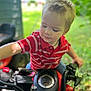 Canaan is registered to the contest to win money with this photo: boy, casual_clothing, child, curious, cute, daylight, face, greenery, leisure, motorbike, nature, outdoor, playtime, portrait, red_shirt, short_hair, summer, toddler, toy_vehicle, young_child