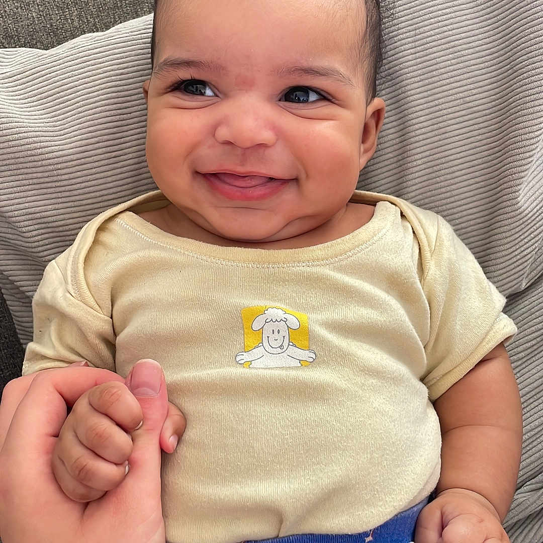 Isaiah participe au concours pour gagner de l'argent avec cette photo : baby, cheeky, closeup, comfort, cushion, cute, expression, face, hair, hand_holding, happy, indoors, infant, pants, patterned_clothing, person, seated, shirt, skin, smiling