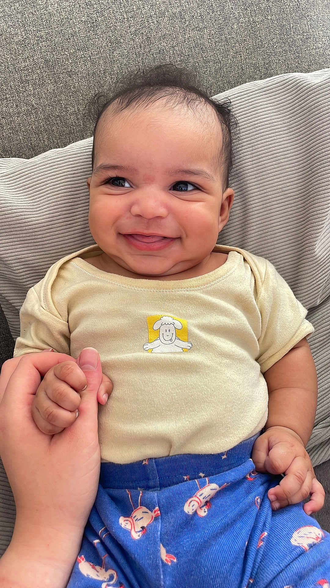 Isaiah participe au concours pour gagner de l'argent avec cette photo : baby, smiling, hand_holding, cushion, shirt, pants, patterned_clothing, infant, happy, cheeky, face, expression, person, cute, indoors, closeup, skin, hair, seated, comfort